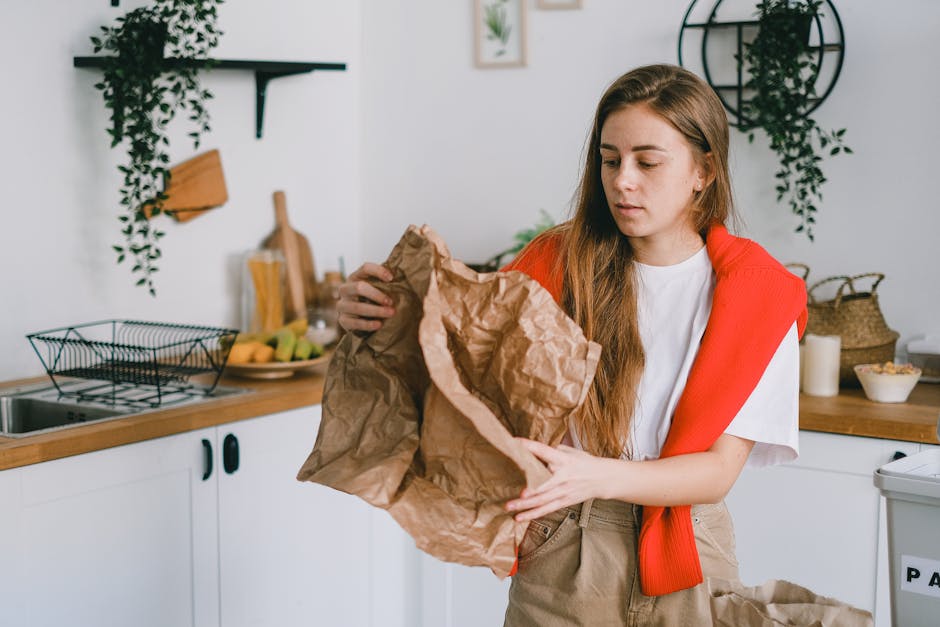 A person's hand and forearm extended from the left side of the image, holding a translucent green plastic bag filled with miscellaneous waste, which appears to contain crumpled paper and other lightwe